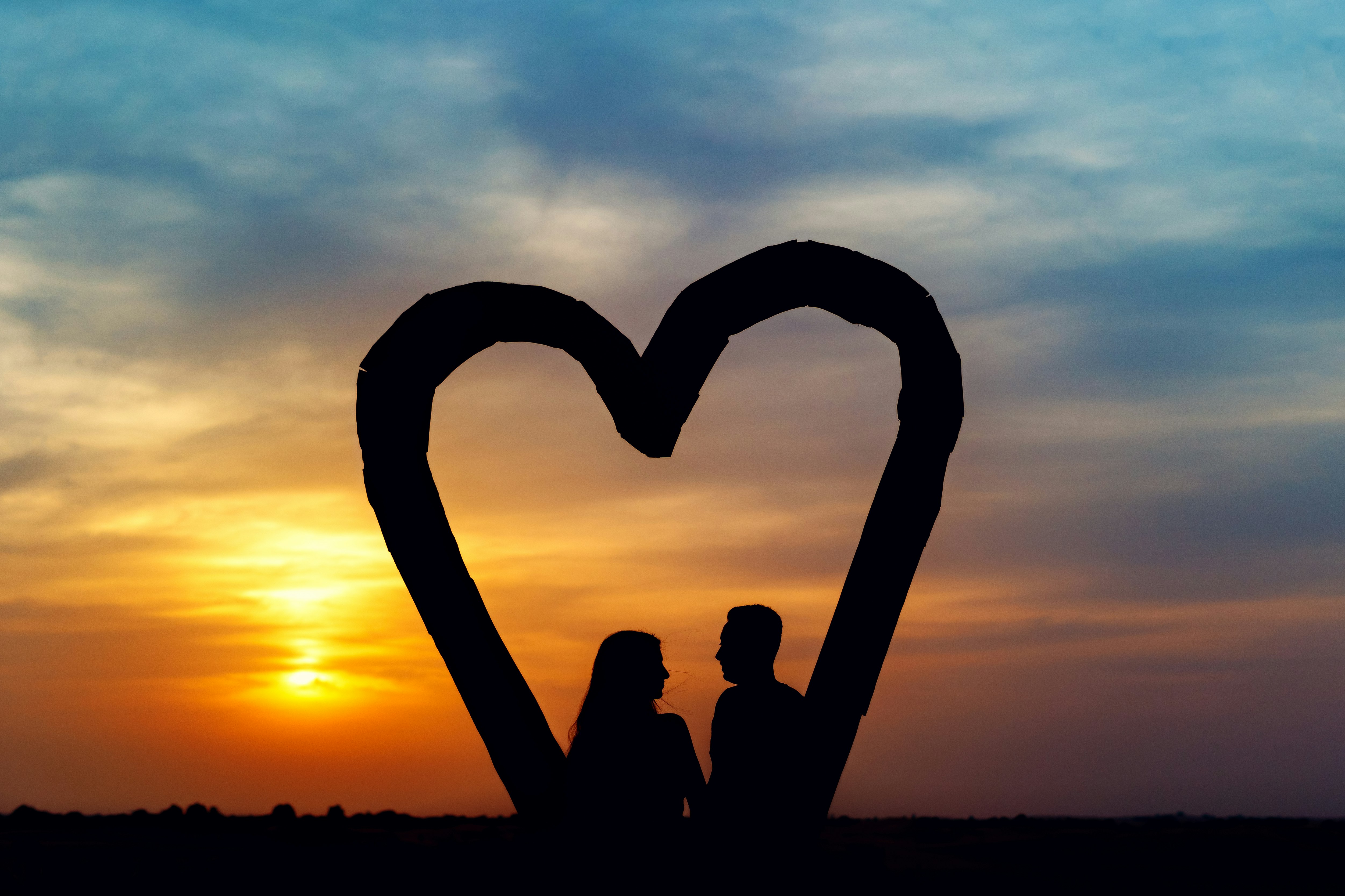 silhouette of 2 people sitting on beach during sunset